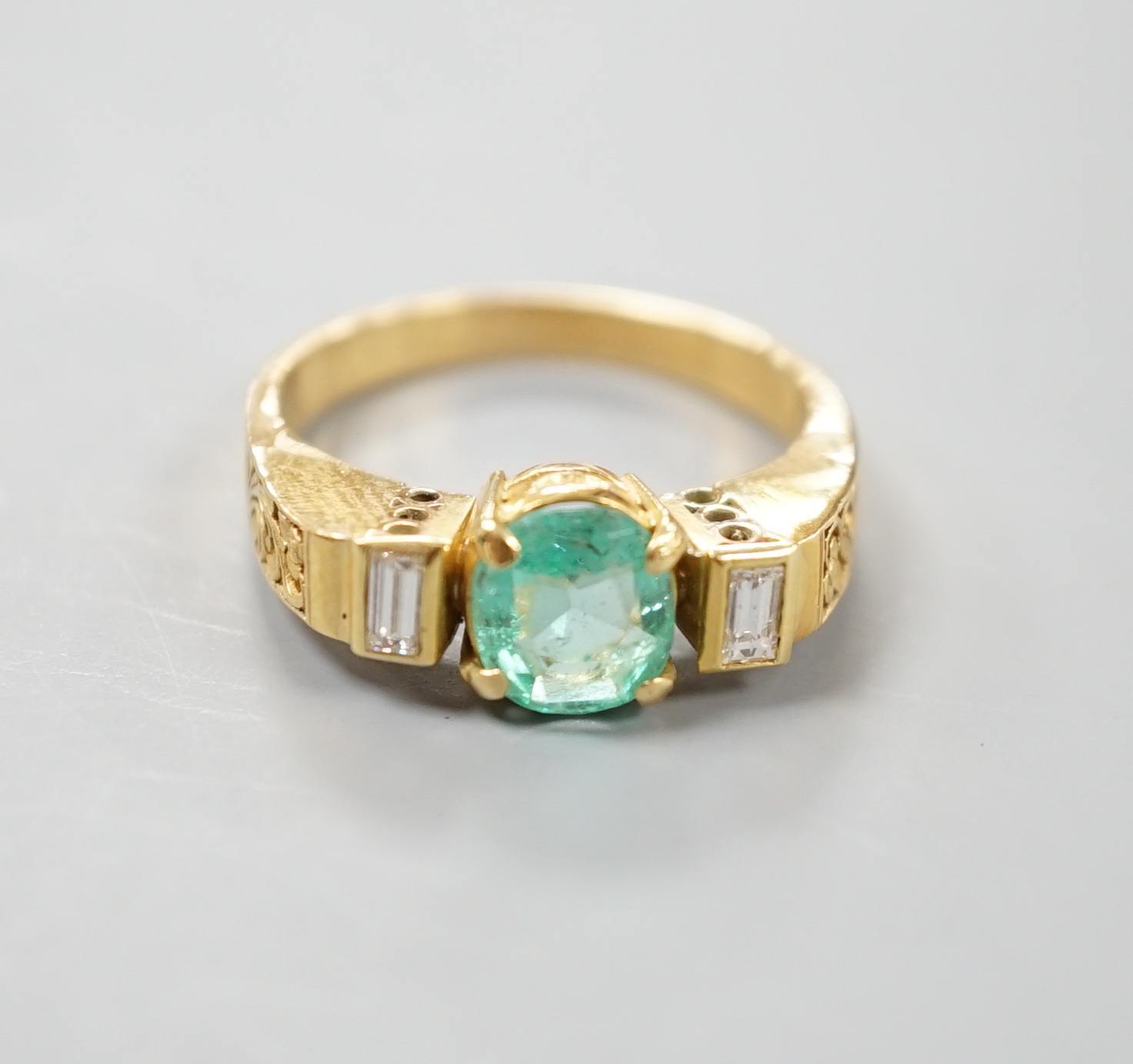 A modern yellow metal, round cut emerald and two stone baguette cut diamond set dress ring, with pierced shoulders, size Q/R, gross 5.5 grams.